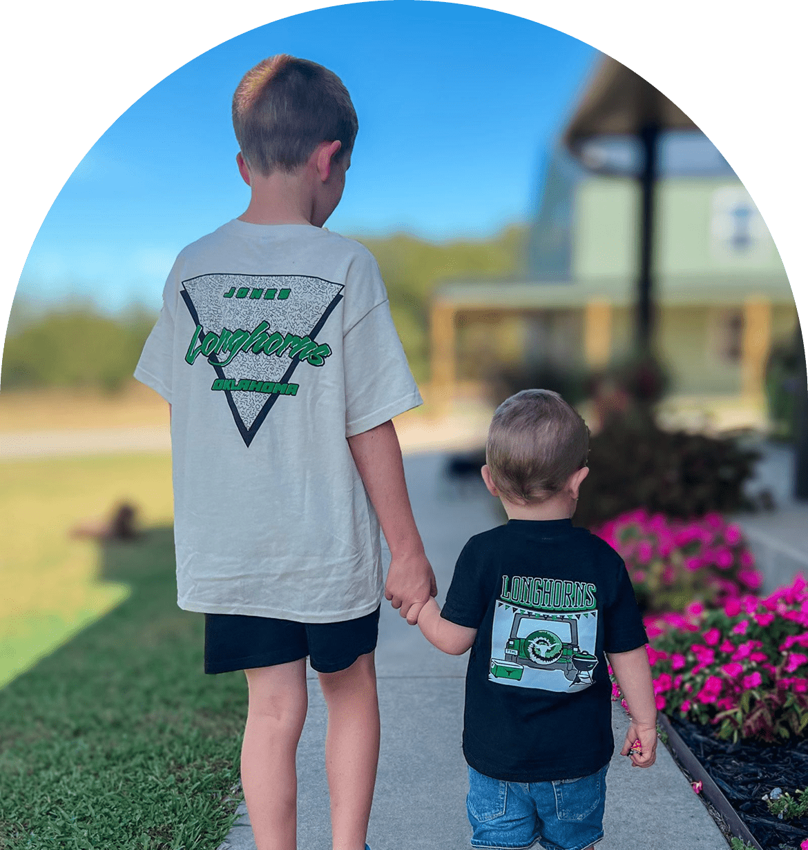 Two children holding hands outside, wearing t-shirts.